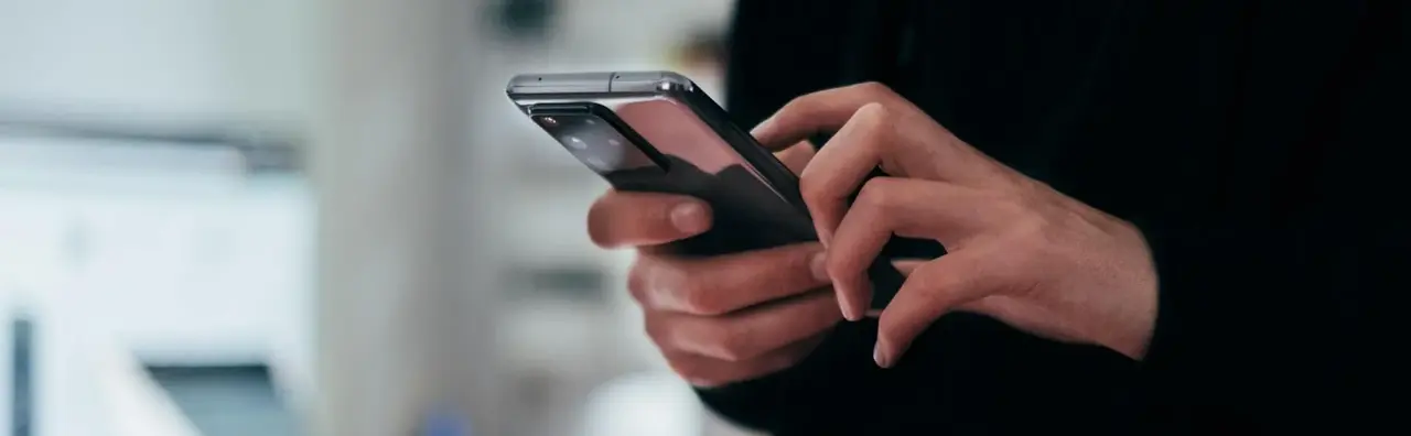 angedeutete Person, die ein handy bedient mit Büro im Hintergrund