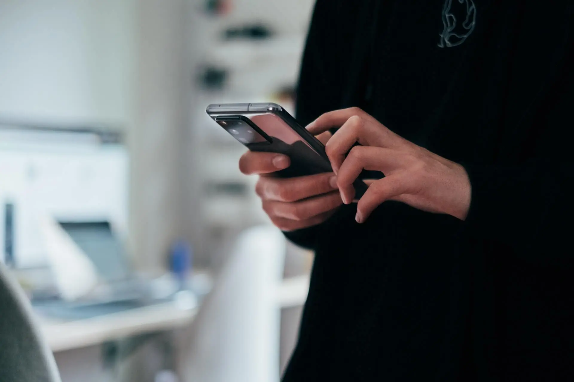 angedeutete Person, die ein handy bedient mit Büro im Hintergrund