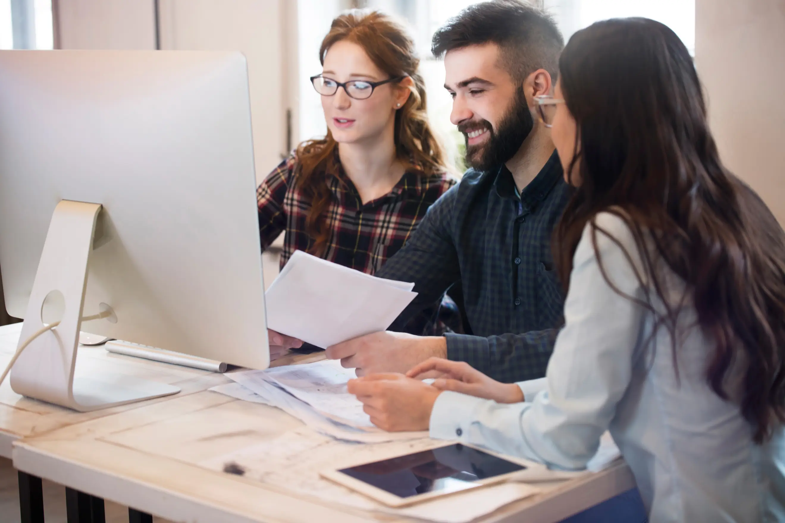 Zwei Frauen und ein Mann sitzen vor einem Bildschirm und arbeiten