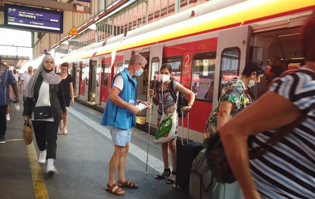 Ein Ehrenamtlicher der Bahnhofsmission hilft einer jungen Frau beim Umsteigen.